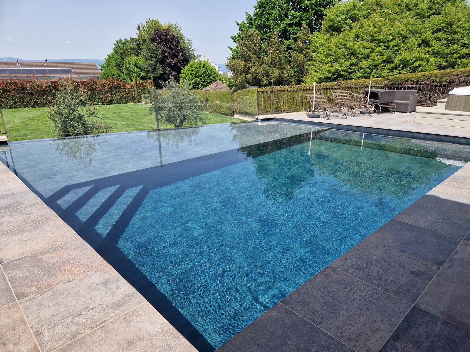 Piscine à débordement avec terrasse en pierre réalisée par Swiss Piscine